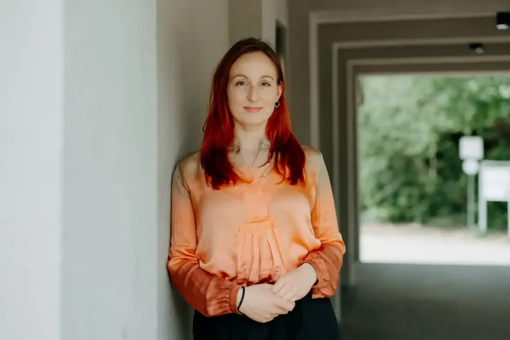 Rotaarige Frau in eleganter Bluse vor einem Fenster