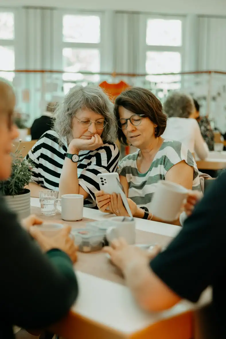 Zwei Frauen betrachten gemeinsam ein Smartphone im Café