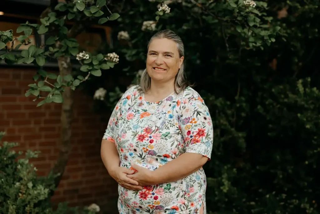 Lächelnde Frau im Blumen-Shirt vor grüner Gartenkulisse