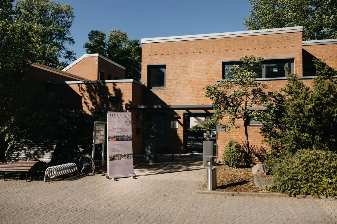 Backsteingebäude mit Eingang, Fahrradständer und Hinweisschild